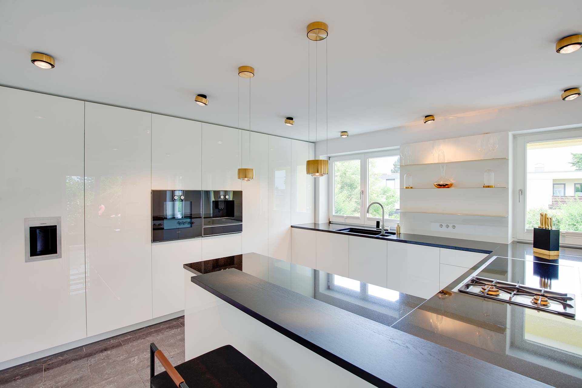 Weiße Hochglanz-Küche mit schwarzer Steinarbeitsplatte und goldenen Details